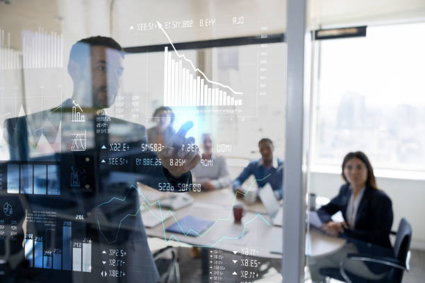 A businessman in a conference room analyzes data on a transparent screen, with colleagues seated at the table.