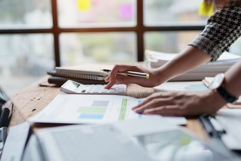 A person using a calculator while reviewing financial documents at a desk.