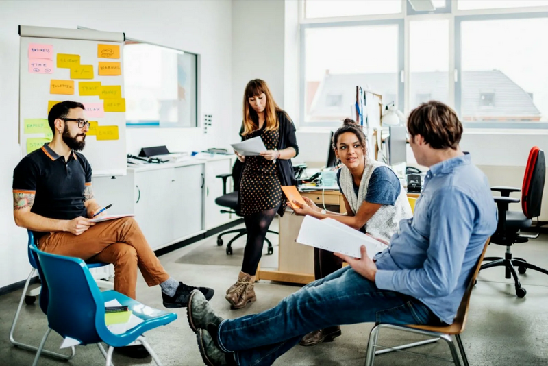 A group of four people engage in a discussion in a modern office setting.